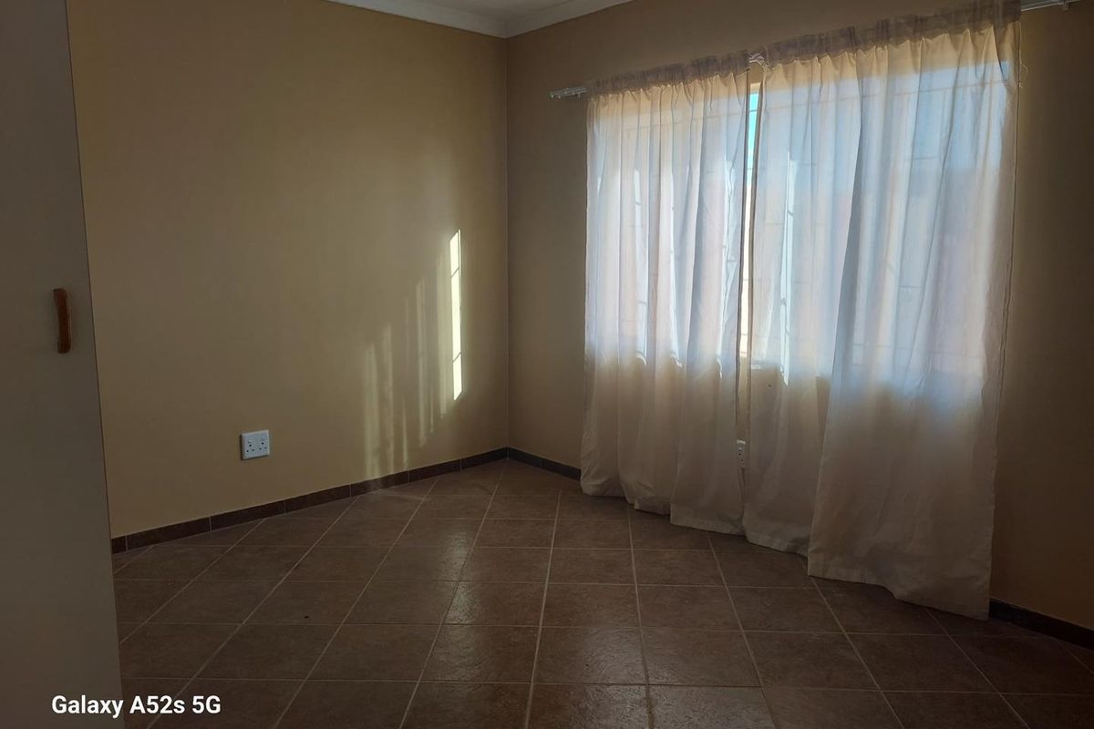 A vacant bedroom featuring neutral wall paint, tiled flooring, and a window fitted with curtain tracks and sheer curtains.