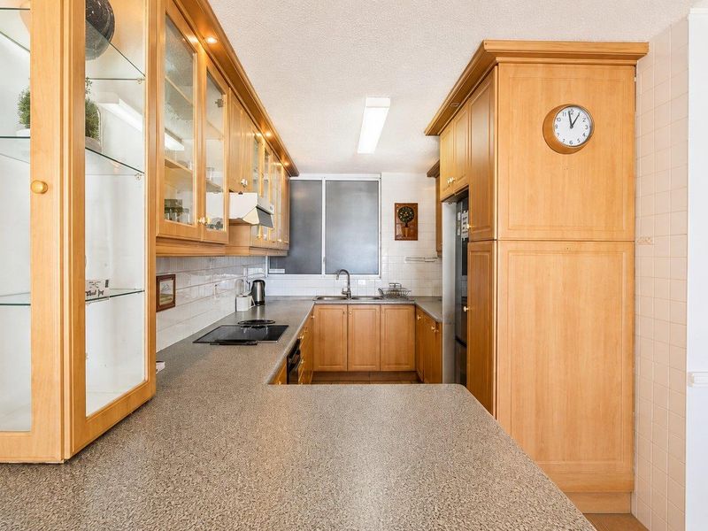 A functional kitchen featuring light wood cabinetry, laminate countertops, built-in appliances, and a tiled backsplash, offering a classic and practical layout.