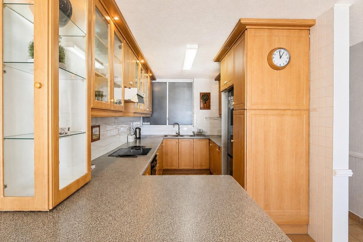 A functional kitchen featuring light wood cabinetry, laminate countertops, built-in appliances, and a tiled backsplash, offering a classic and practical layout.