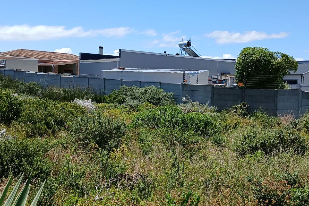 A view of the rear boundary of the vacant residential plot, featuring a precast concrete wall with electric fencing and neighbouring property structures.