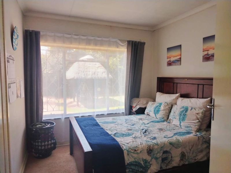 A standard bedroom featuring carpeted flooring and a large window fitted with security bars, offering a view of the garden area.