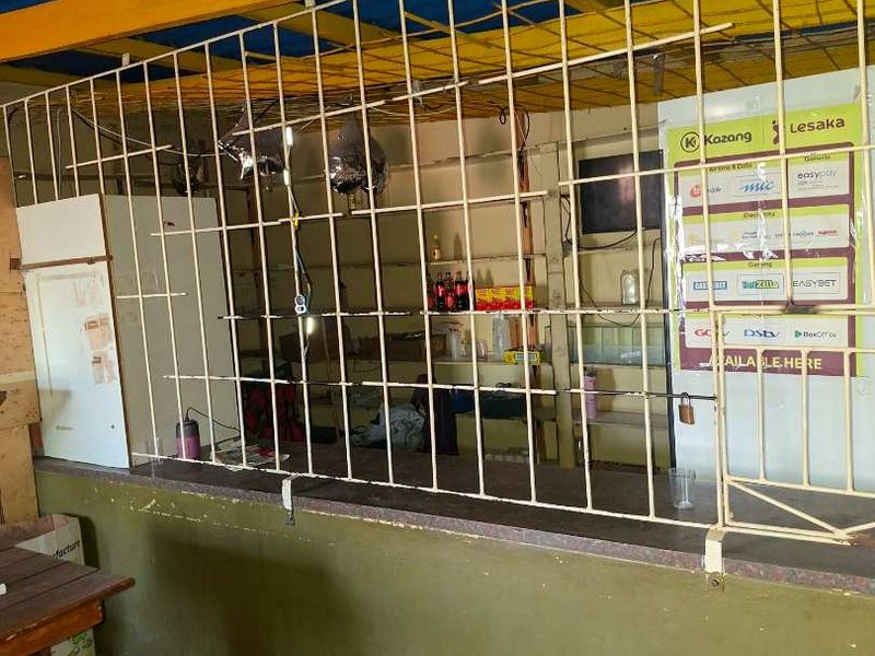 A service kiosk or utility area featuring a security grille, service counter, and exposed roof structure, currently used for commercial service transactions.