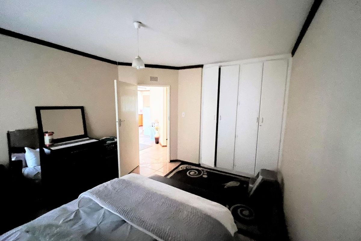 A bedroom featuring built-in cupboards and a doorway leading to an adjacent living area.