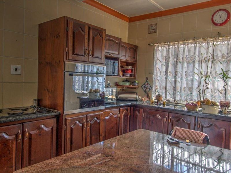 A traditional kitchen featuring dark wood cabinetry, granite countertops, built-in oven, and hob, with fully tiled walls.