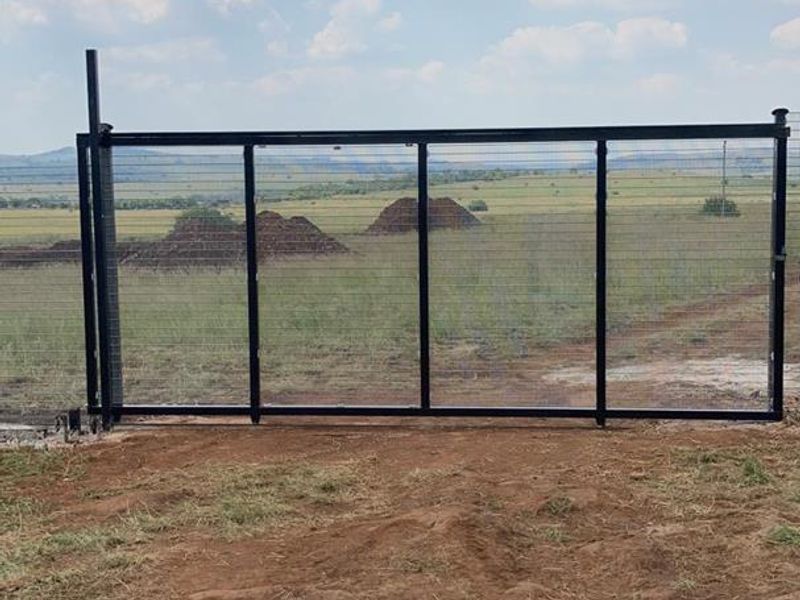 A secure metal sliding gate with wire mesh fencing installed at the entrance of the vacant agricultural land.