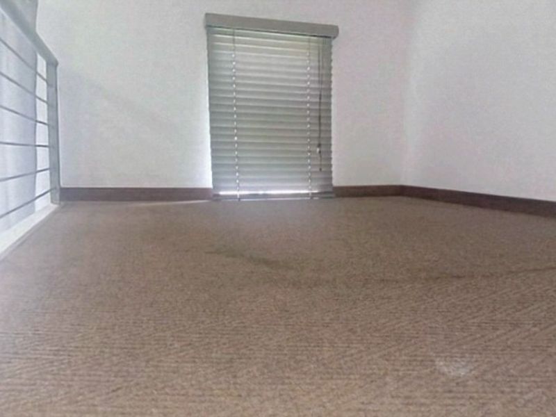 An empty loft-style bedroom area featuring carpeted flooring, a metal balustrade, and window blinds.