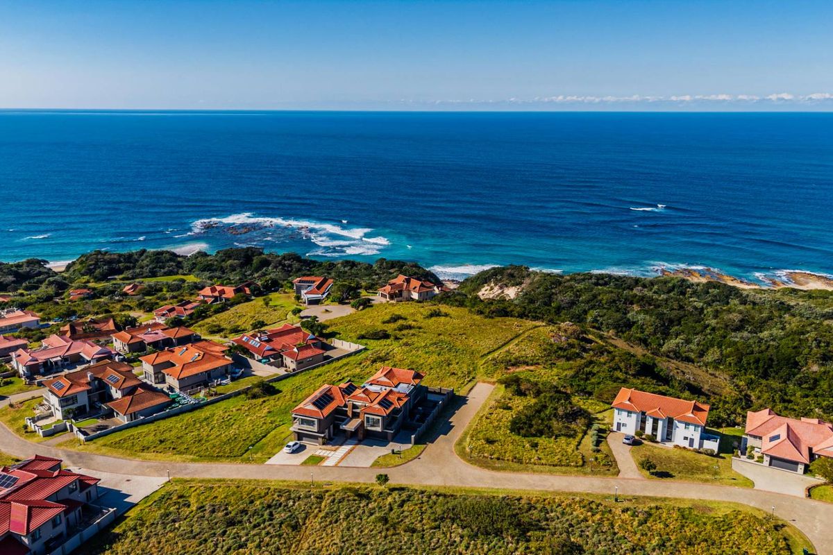 An aerial view of a coastal residential estate featuring multiple homes with tiled roofs, solar panels, and paved access roads overlooking the ocean.