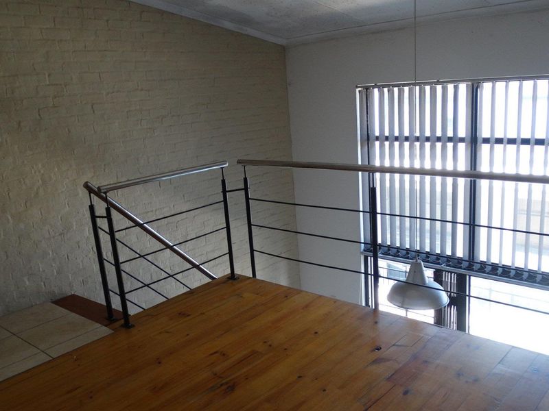 An open mezzanine level featuring timber flooring, a modern stainless steel balustrade, and an exposed brick wall with large windows and vertical blinds.
