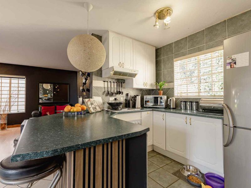 Open-plan kitchen featuring white cabinetry, dark laminate countertops, a breakfast bar, and tiled flooring, seamlessly connecting to the adjacent living area.