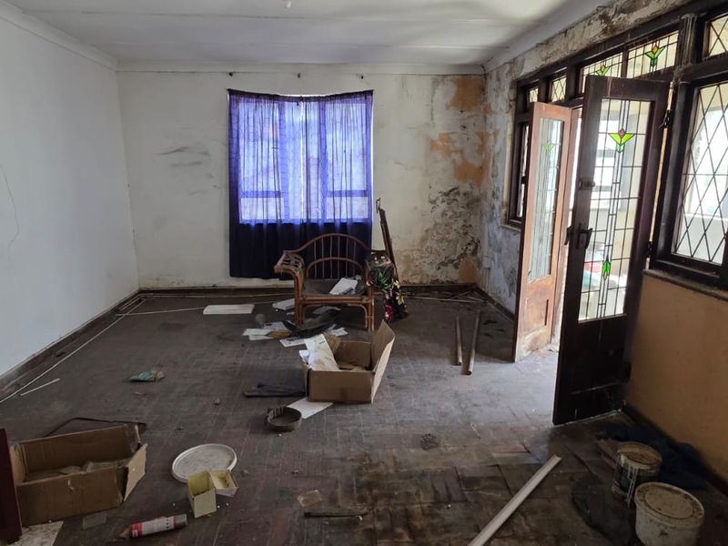 A spacious living room requiring significant renovation, featuring original parquet flooring, leaded glass doors, and timber window frames, currently in a state of disrepair.