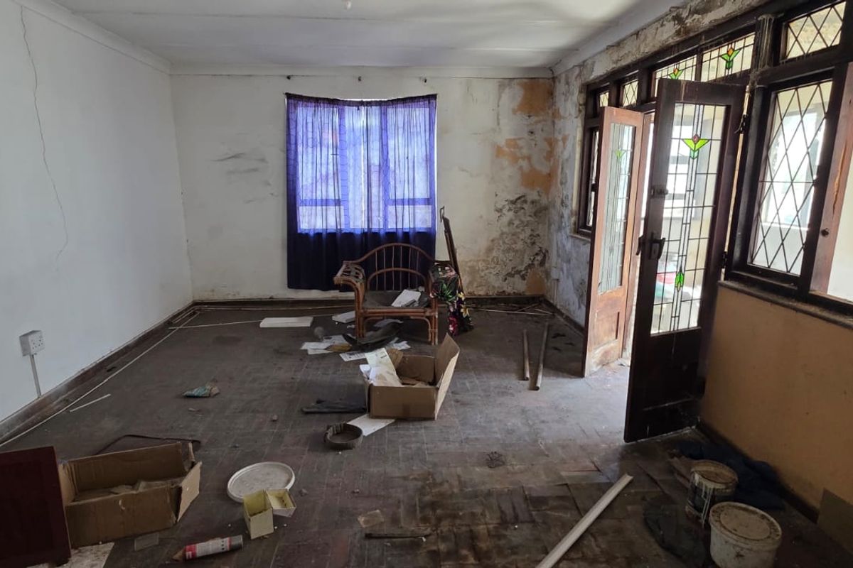 A spacious living room requiring significant renovation, featuring original parquet flooring, leaded glass doors, and timber window frames, currently in a state of disrepair.