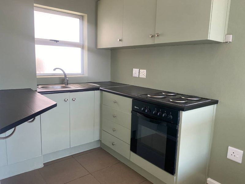 A functional kitchen featuring sage green cabinetry, dark countertops, a built-in oven with electric hob, and tiled flooring.