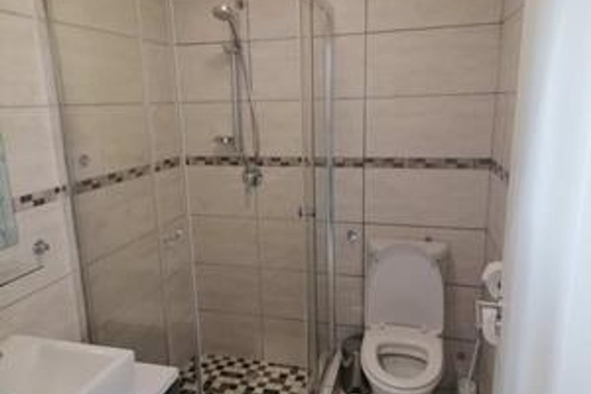A compact hotel bathroom featuring a glass-enclosed shower, a wall-mounted toilet, and a modern vanity basin with tiled walls and flooring.