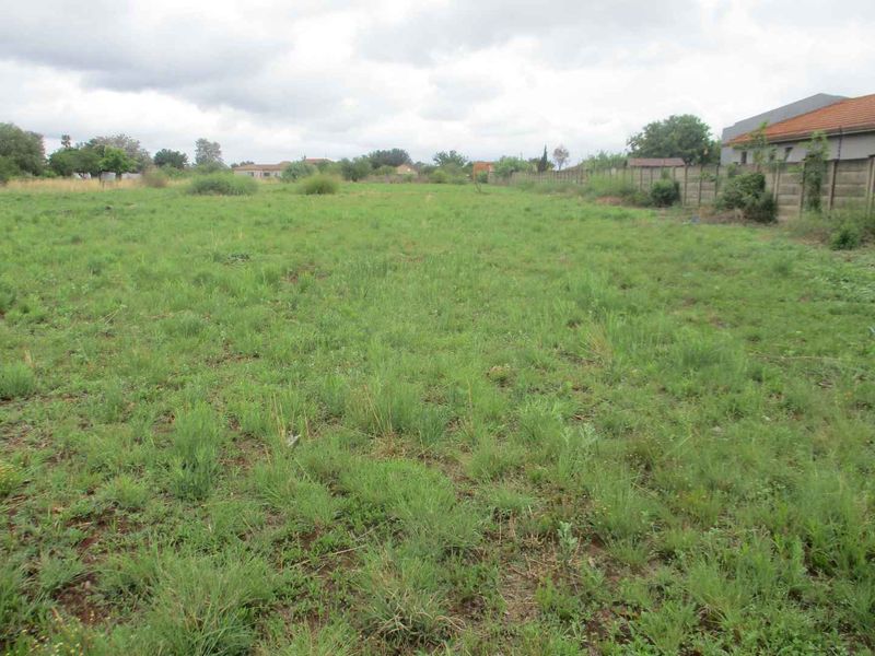 A vacant residential plot featuring open grassland and a perimeter boundary wall, offering a blank canvas for future development.