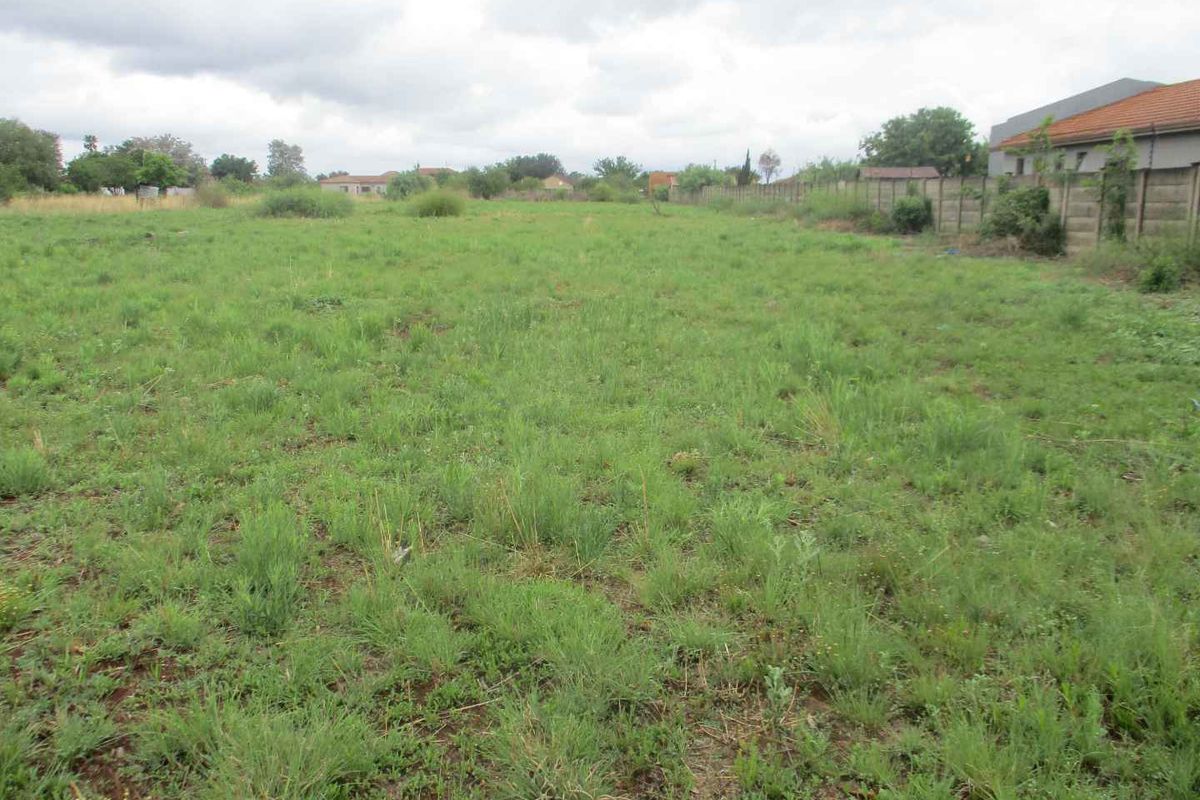 A vacant residential plot featuring open grassland and a perimeter boundary wall, offering a blank canvas for future development.