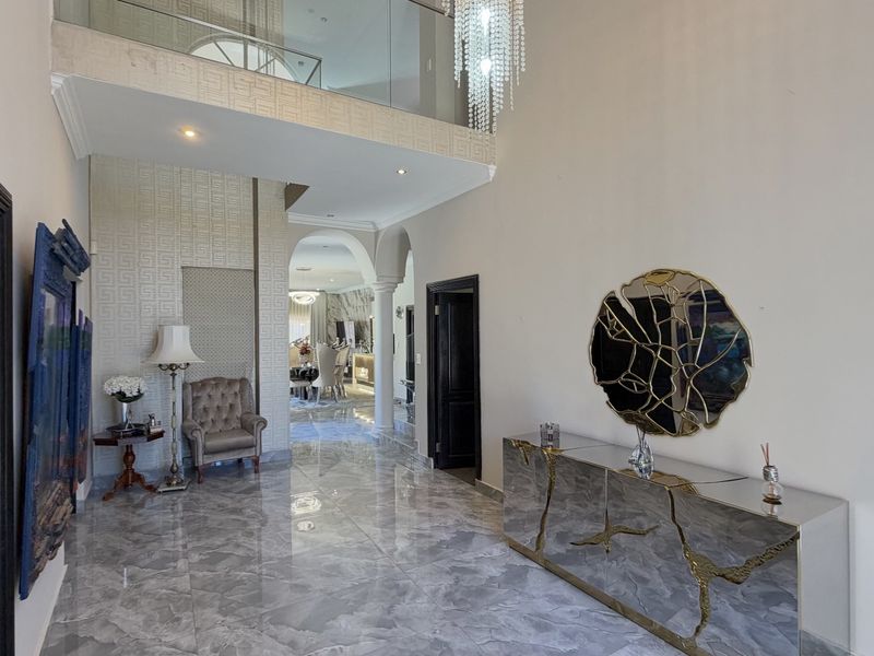 Grand double-volume entrance hall featuring polished marble flooring, a glass balustrade mezzanine, and elegant architectural archways leading to the main living areas.