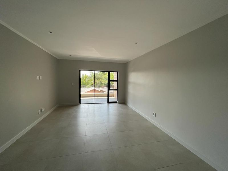 A bright, spacious, and empty living area featuring neutral tiled flooring, recessed lighting, and a large sliding glass door leading to an outdoor space.
