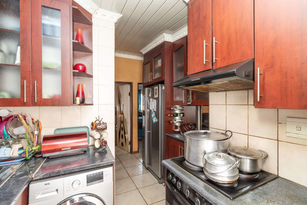 A functional kitchen featuring dark wood cabinetry, tiled splashbacks, and integrated appliances, offering a practical layout with potential for modern cosmetic updates.