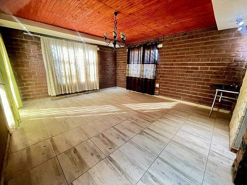 Spacious living area featuring exposed brick walls, a warm timber plank ceiling, and modern tiled flooring, offering a unique rustic aesthetic.