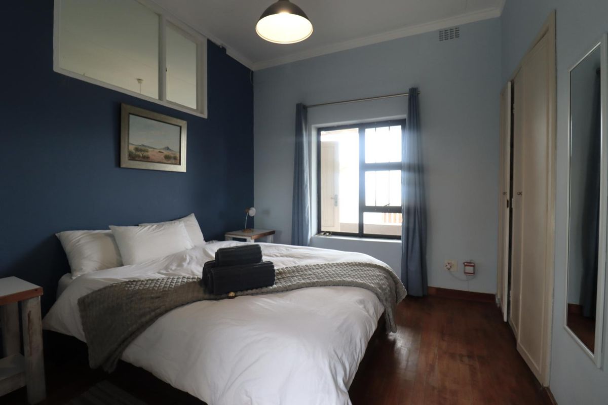 A bedroom featuring dark blue accent wall, timber flooring, built-in cupboards, and a transom window providing additional natural light.