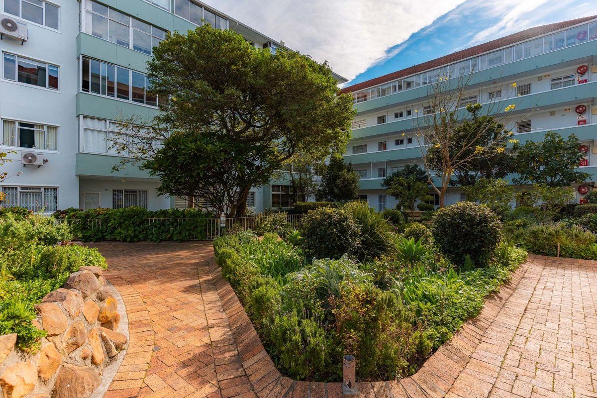 A well-maintained communal garden area featuring brick pathways, mature trees, and landscaped beds set between multi-story apartment building facades.