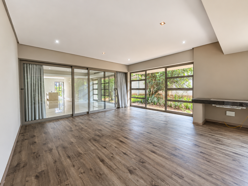 Spacious, light-filled living area featuring modern laminate flooring, recessed lighting, and large sliding glass doors that open to a private garden view.