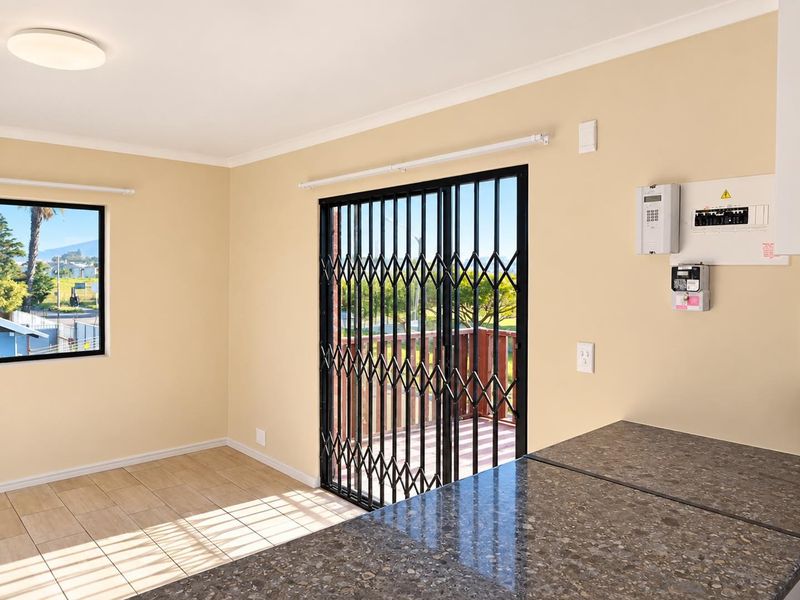 Bright open-plan living area featuring tiled floors, granite countertops, and a sliding door with security gate leading to an outdoor deck.