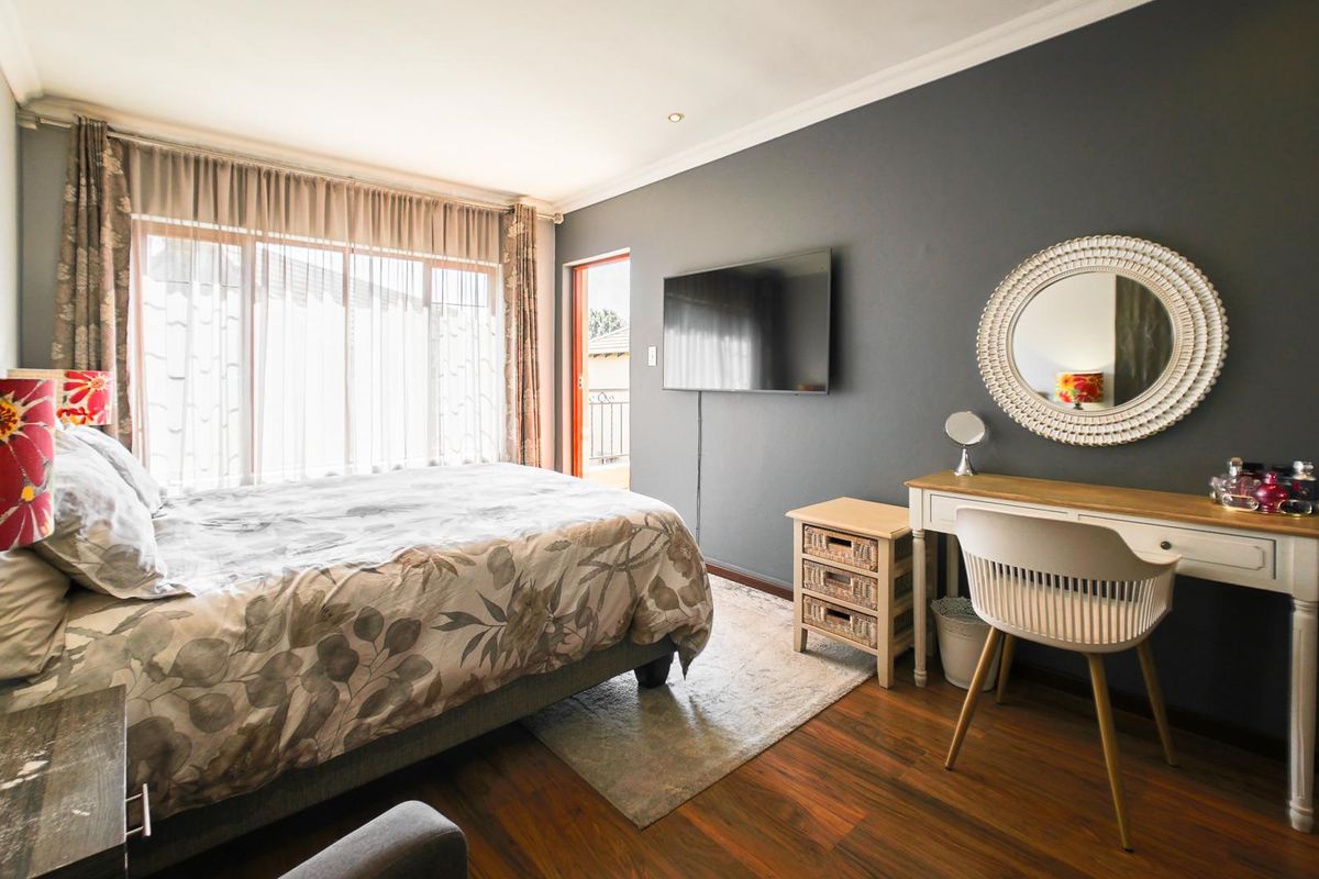 A well-lit bedroom featuring hardwood flooring, crown molding, and direct access to a balcony through a sliding glass door.