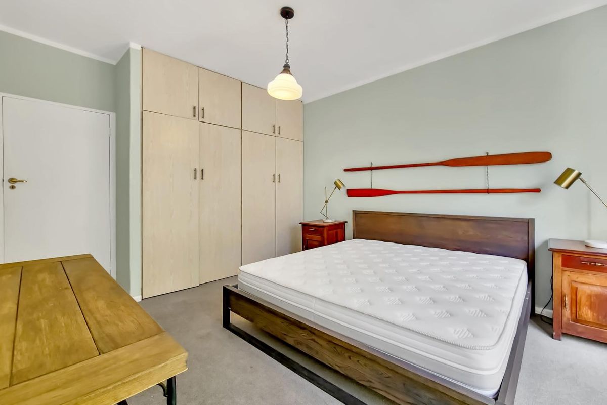A well-maintained bedroom featuring neutral wall tones, carpet flooring, and ample storage provided by floor-to-ceiling built-in wardrobes.