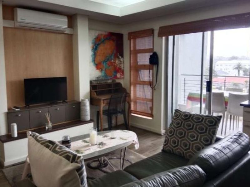 A comfortable living room featuring a built-in media console, split-system air conditioning, and direct access to a balcony through sliding glass doors.