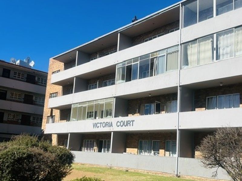 Exterior view of Victoria Court apartment building featuring multi-story balconies, large windows, and surrounding landscaped garden area.