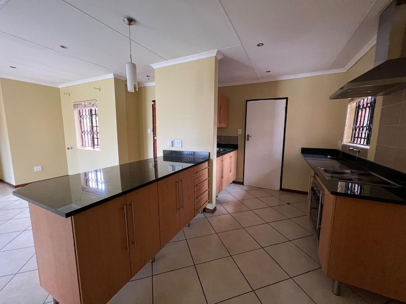 Spacious kitchen featuring granite countertops, built-in cabinetry, integrated oven, and extractor fan, with tiled flooring and security bars on windows.