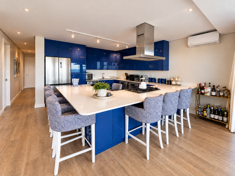 Modern open-plan kitchen featuring high-gloss blue cabinetry, a large central island with quartz countertops, integrated appliances, and contemporary lighting.