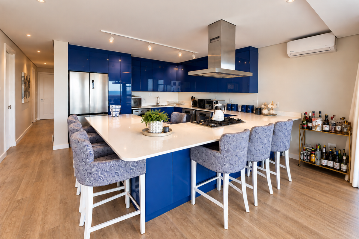 Modern open-plan kitchen featuring high-gloss blue cabinetry, a large central island with quartz countertops, integrated appliances, and contemporary lighting.