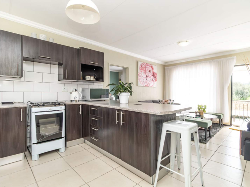 Open plan kitchen and living area featuring dark wood cabinetry, gas stove, tiled flooring, and direct access to an outdoor balcony.