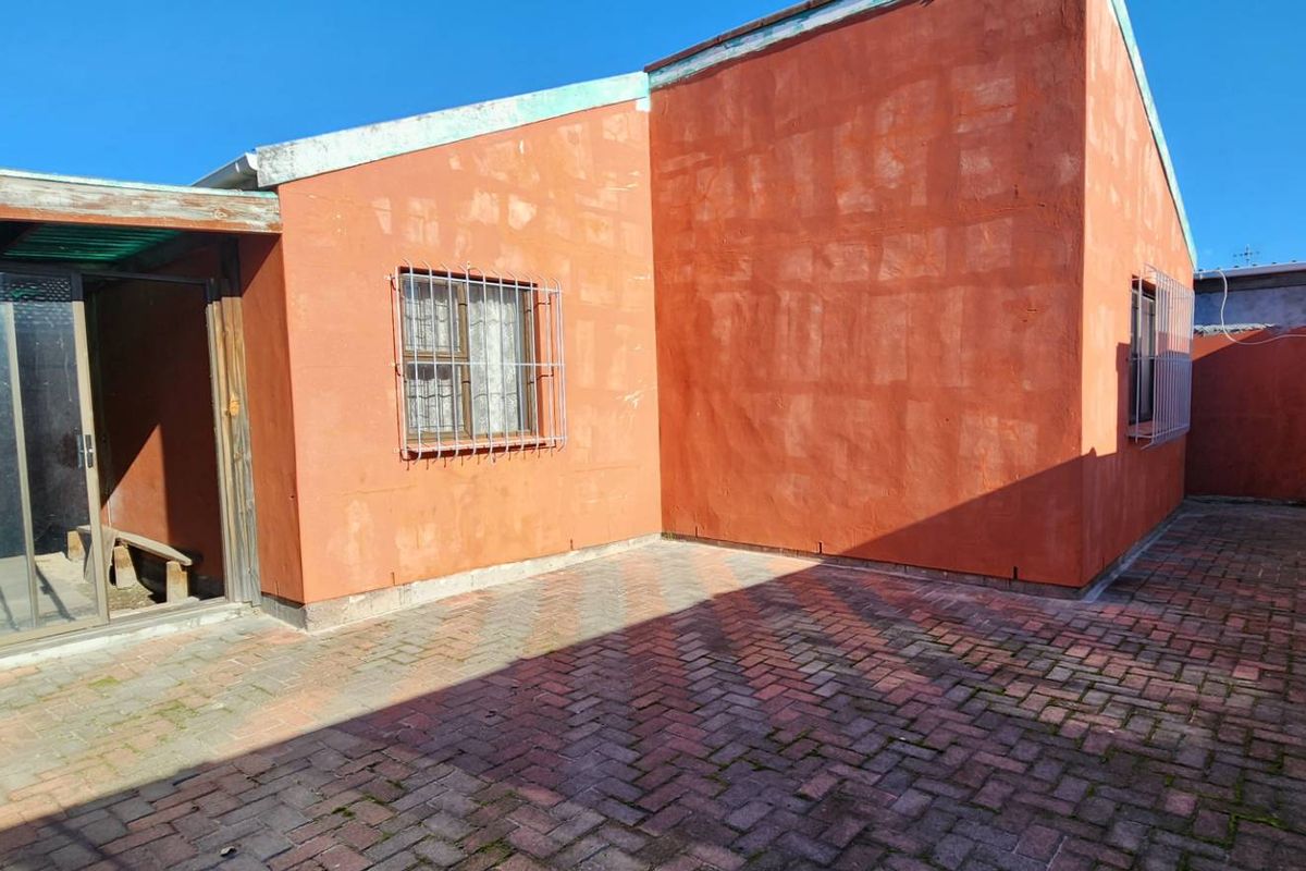 Rear exterior view of the property featuring a paved courtyard, sliding glass doors, and security bars on windows.