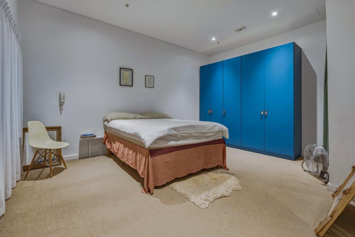 A spacious bedroom featuring neutral carpeting, recessed downlighting, and a large, vibrant blue built-in wardrobe providing ample storage space.
