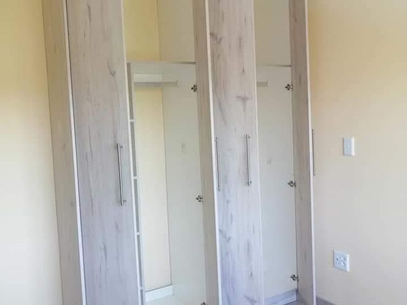 A bright bedroom featuring modern light wood-finish built-in wardrobes and neutral tiled flooring.