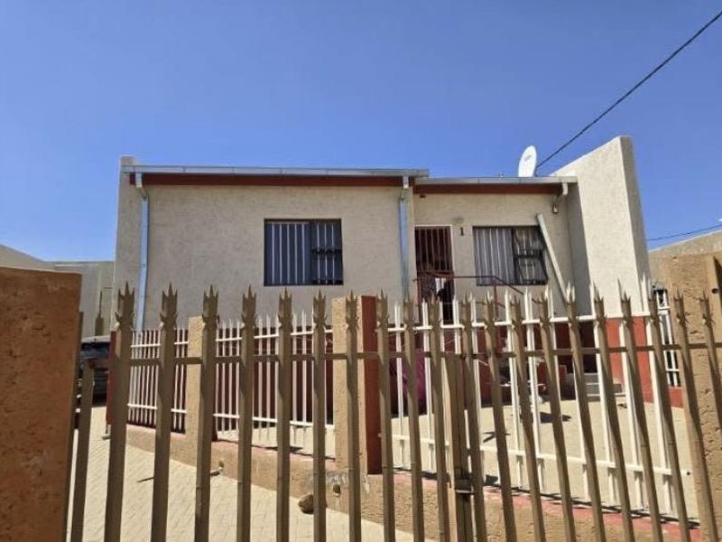 Front elevation of a townhouse featuring a paved driveway, secure metal fencing, and window security bars.