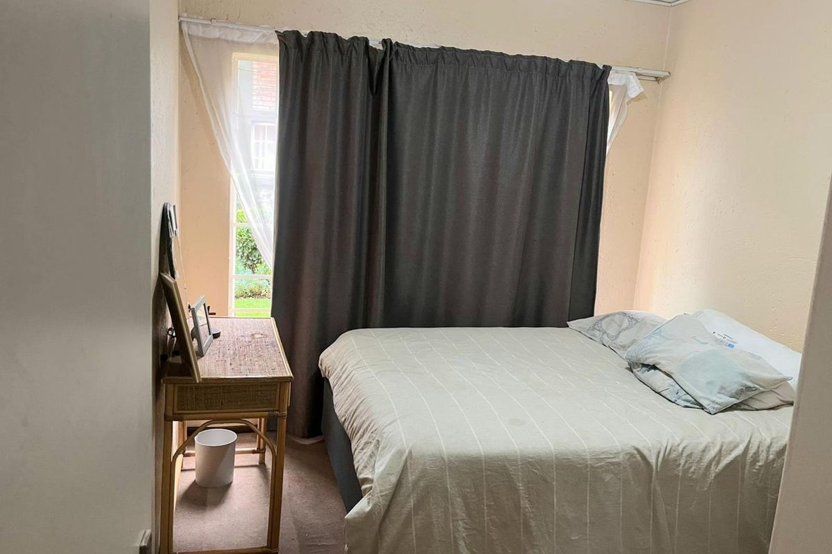 A compact bedroom featuring neutral wall tones, carpeted flooring, and a window with curtain fixtures.