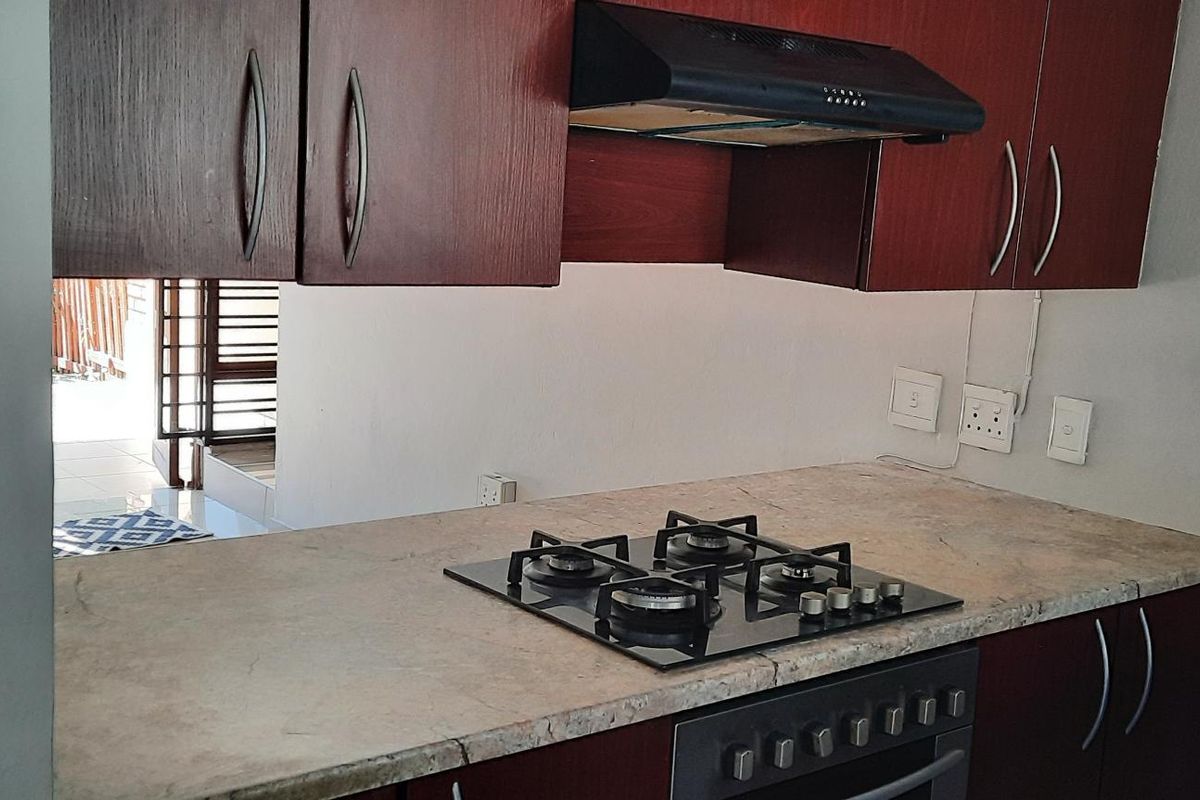 A functional kitchen area featuring dark wood-finish cabinetry, a built-in gas hob, extractor fan, and oven with stone-look countertops.