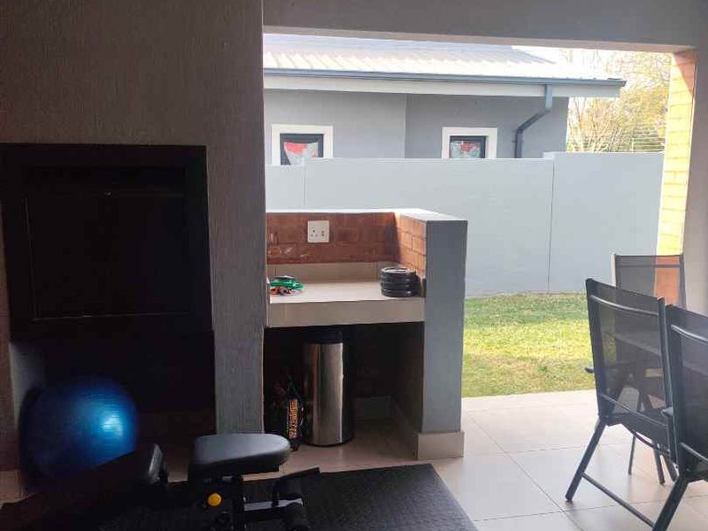 Covered patio area featuring a built-in braai, brick prep counter, and tiled flooring, overlooking the rear garden.