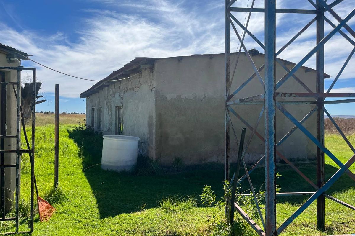 Exterior view of a farm outbuilding showing weathered plaster walls and a large metal tower structure on the property grounds.