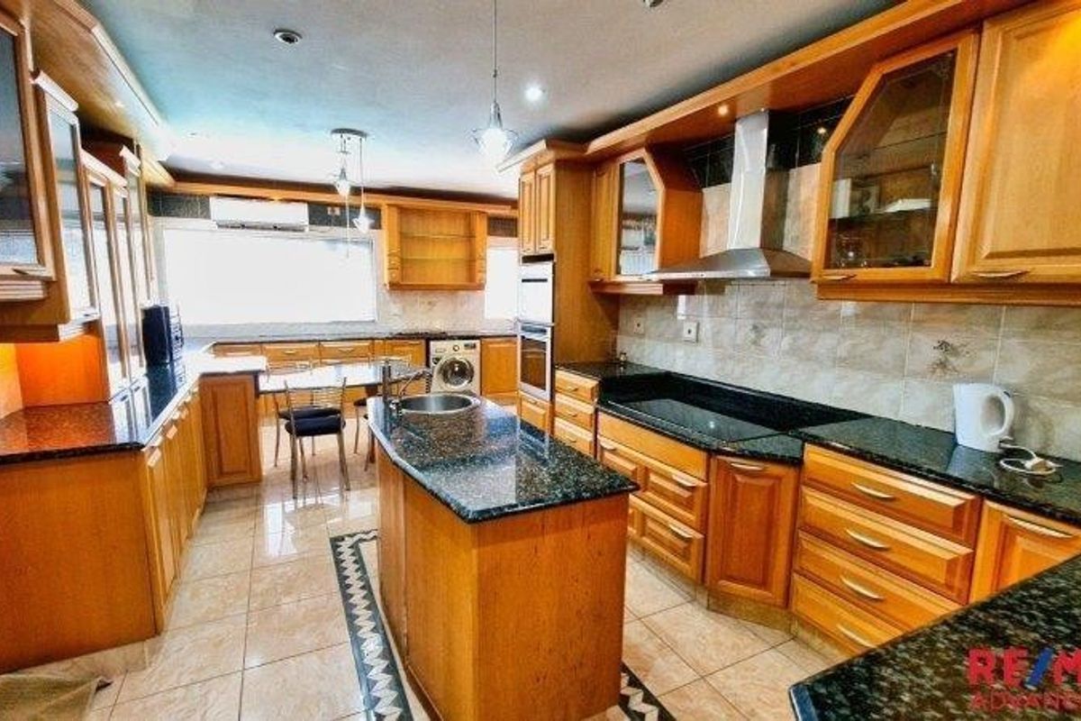 Spacious kitchen featuring extensive wooden cabinetry, granite countertops, a central island, and integrated appliances, offering a functional layout with ample storage and workspace.