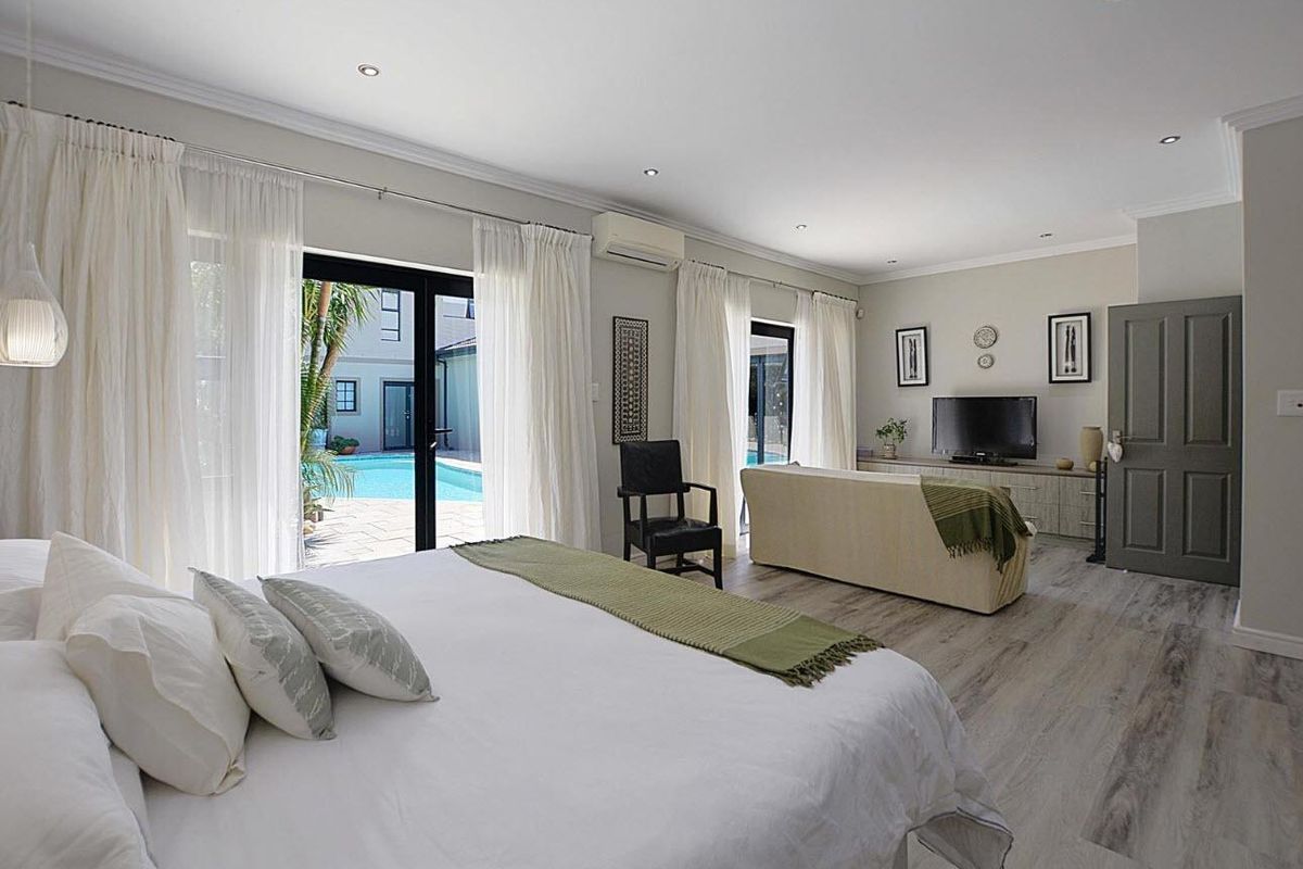Spacious bedroom featuring wood-look flooring, recessed lighting, and large glass sliding doors providing direct access to the outdoor pool area.