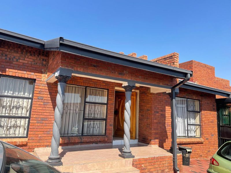 Front facade of a face brick house featuring a covered porch with decorative spiral columns and secure window bars.