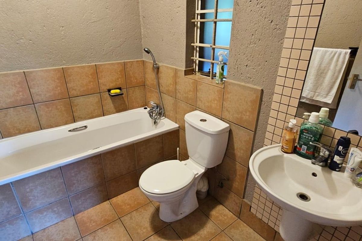 A functional bathroom featuring a bathtub, pedestal basin, and toilet with neutral tiled finishes and a wall-mounted mirror.