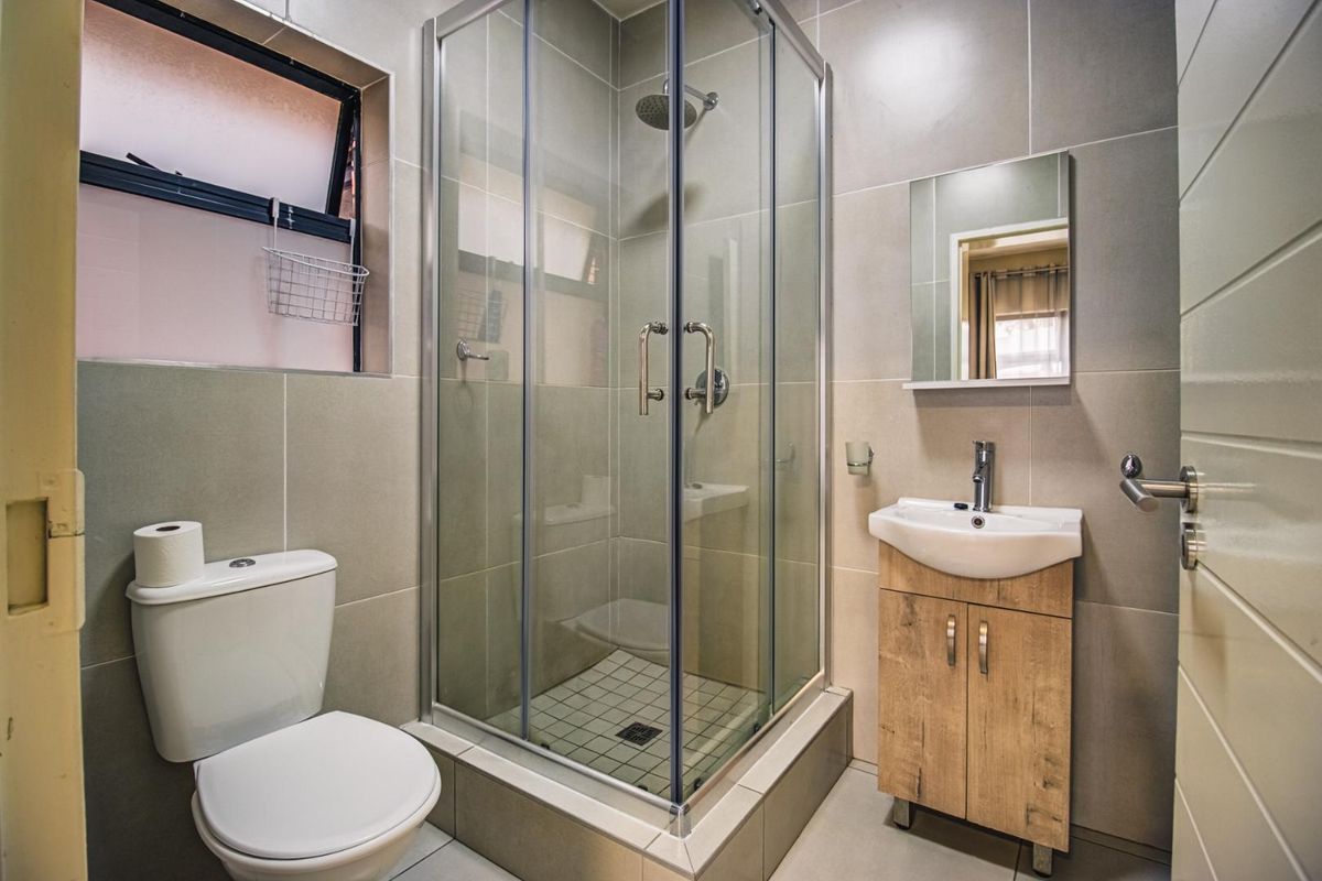 A modern, well-maintained bathroom featuring a glass-enclosed shower, a vanity unit with a basin, and neutral floor-to-ceiling tiling.