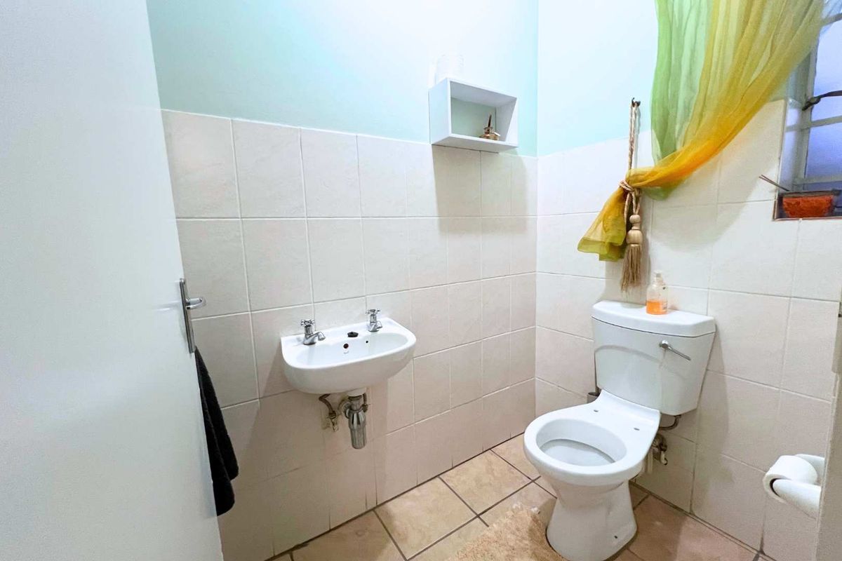 A compact guest bathroom featuring a wall-mounted basin and a standard toilet with neutral wall tiling.