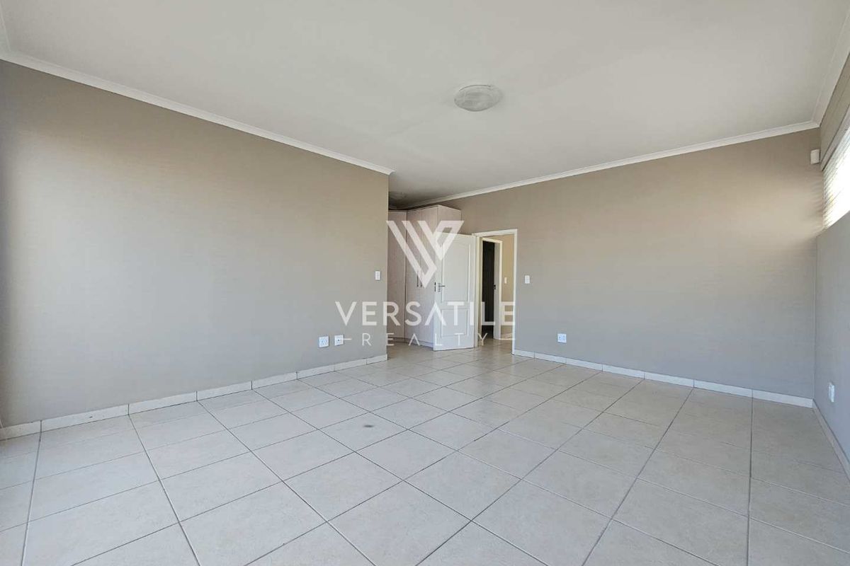 A spacious, empty living area featuring neutral tiled flooring, coved ceilings, and built-in storage cupboards, offering a clean and versatile blank canvas.